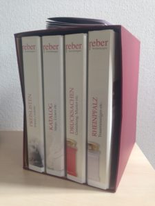 Abbildung eines dunkelroten Schubers mit vier Ring-Ordnern Kataloge: Beispiel von Corporate Design für Reber Bestattungen, Landau